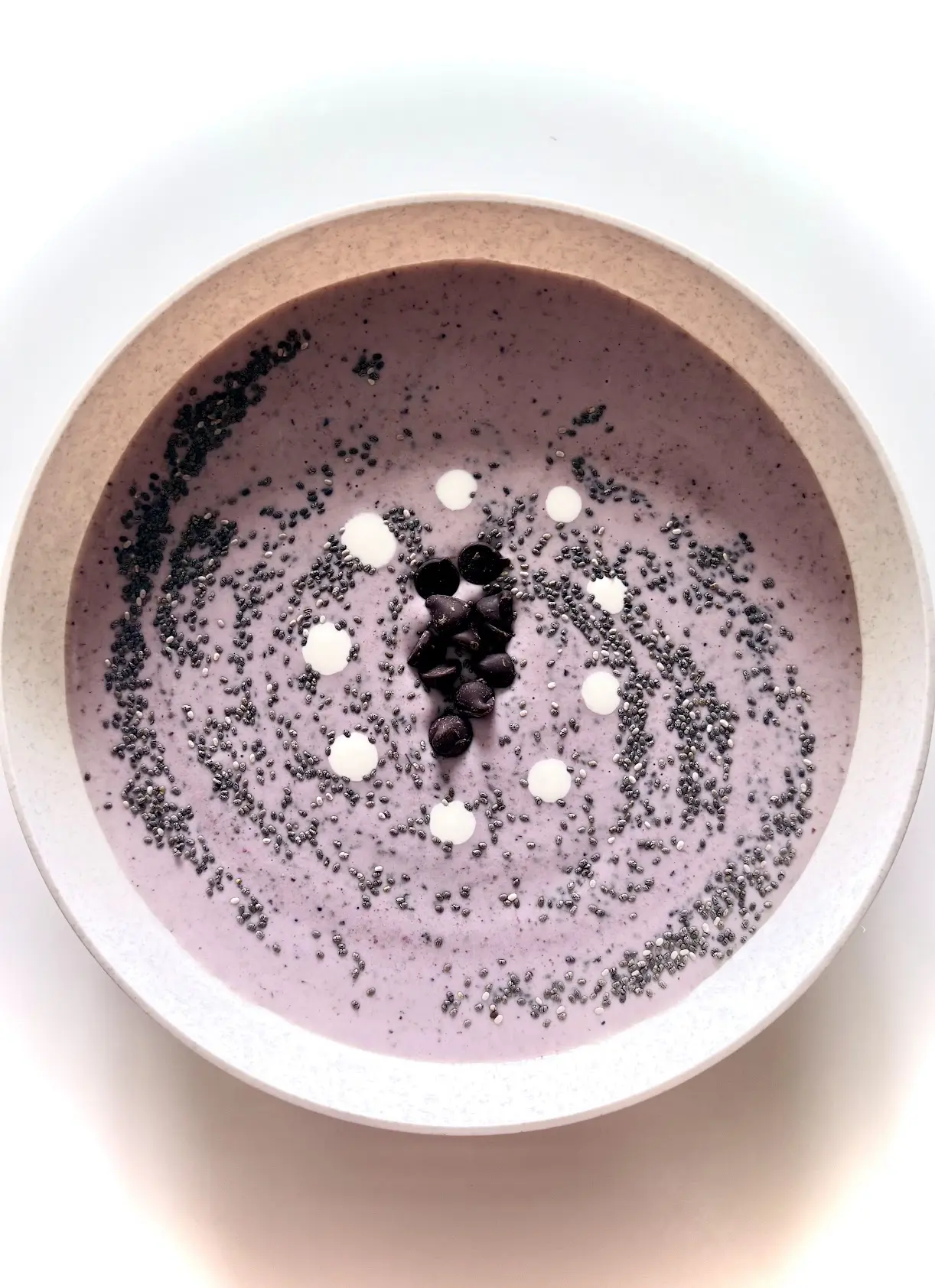 mixed berries smoothie in a bowl topped with chocolate chips and fresh cream droplets